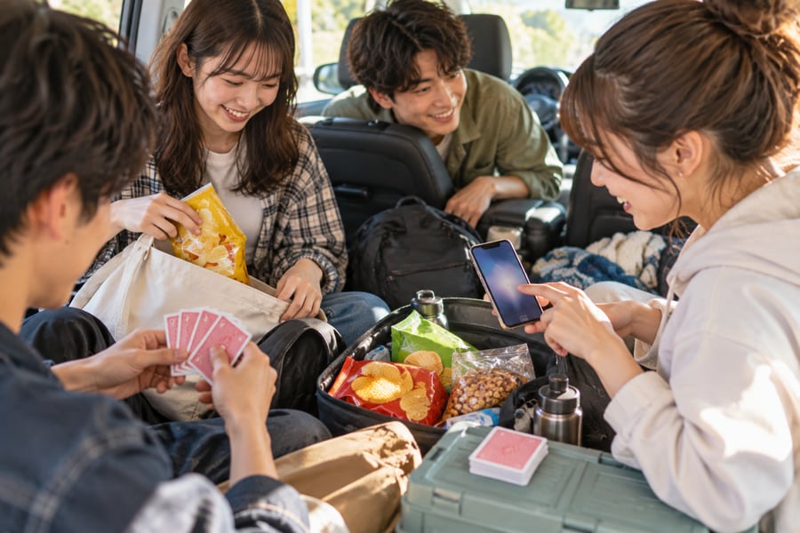出発前の車内で、トランプやおやつ、スマホを用意して移動中の楽しみを準備する友人グループ