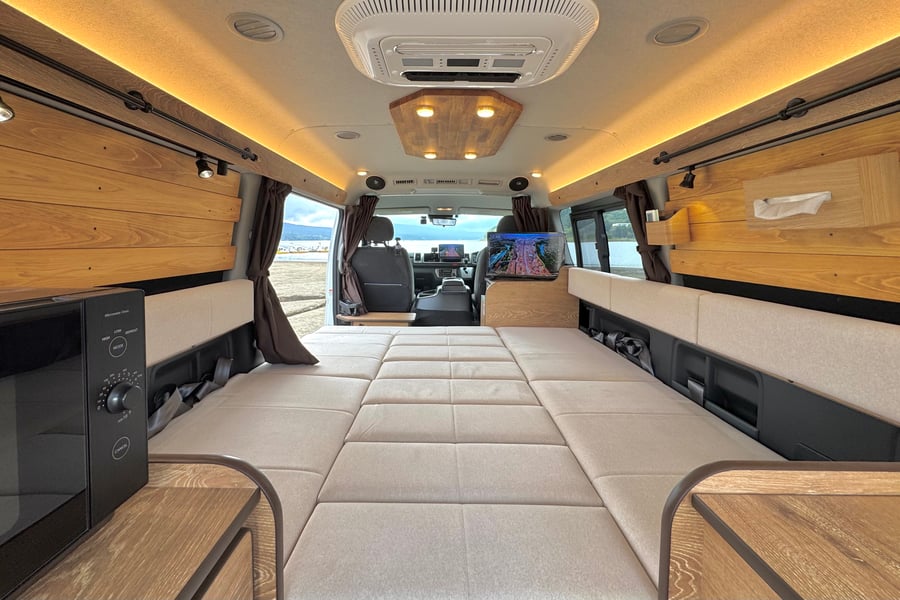 BESのキャンピングカーのソファを広げた状態。車内後方まで白いフラットな就寝スペースが続いている